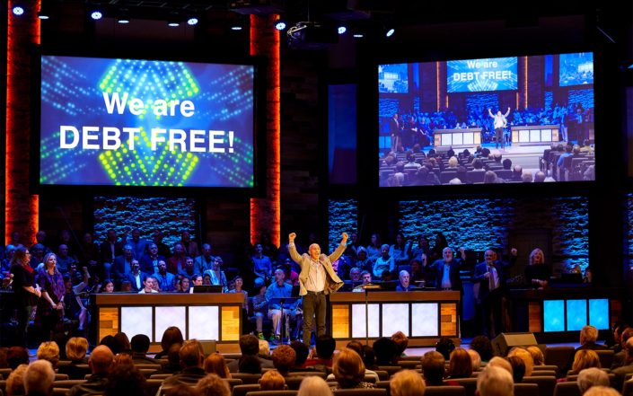 The Village Congregation with "We are DEBT FREE" on Screen