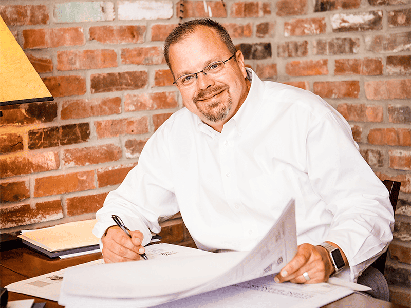 John Torgerson Smiling with a Pencil and Architectural Plans on desk