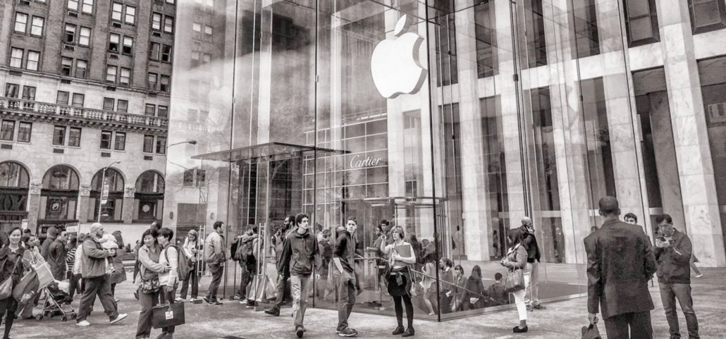 Sepia tone image of several people walking in and out of an apple store in a large city