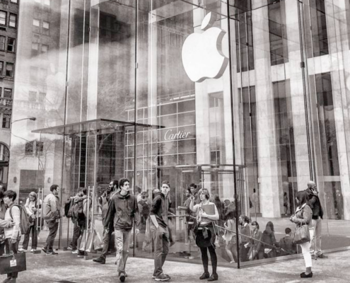 Sepia tone image of several people walking in and out of an apple store in a large city