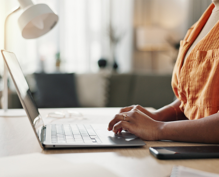 Side view of a woman in an orange shirt typing on a laptop