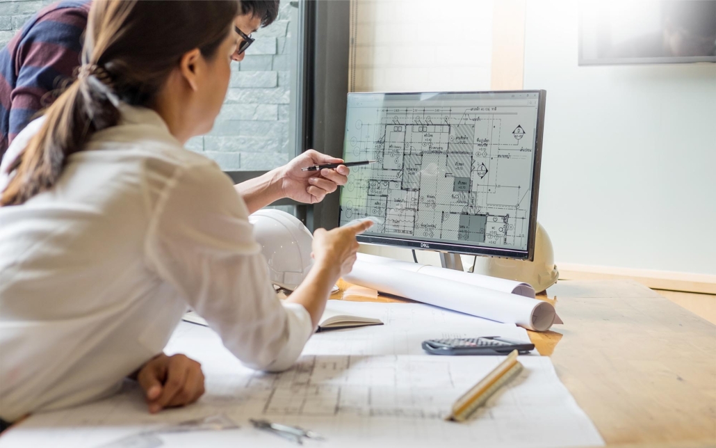 Two engineers looking over architectural blueprints on computer