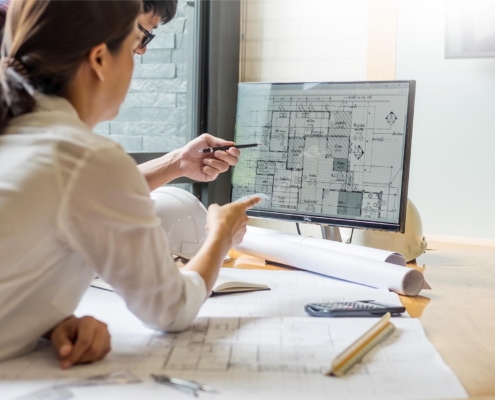 Two engineers looking over architectural blueprints on computer